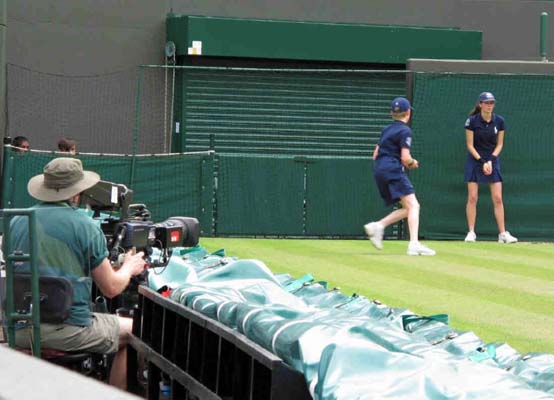 Bollpojkarna och bollflickorna samlar in bollarna, samtidigt som en kameraman tar bilder i Wimbledon.